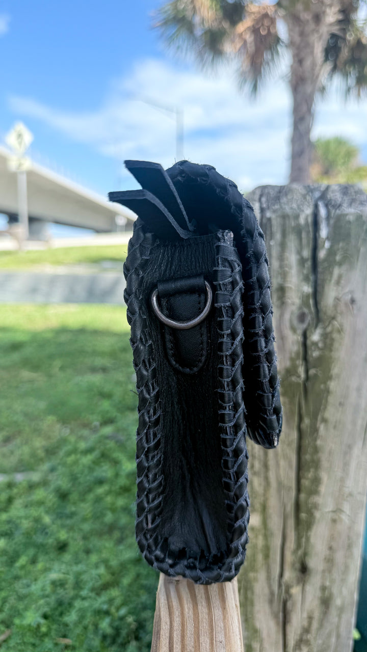Side profile of handmade black leather crossbody purse showing whipstitch edges, metal strap ring and structured shape.