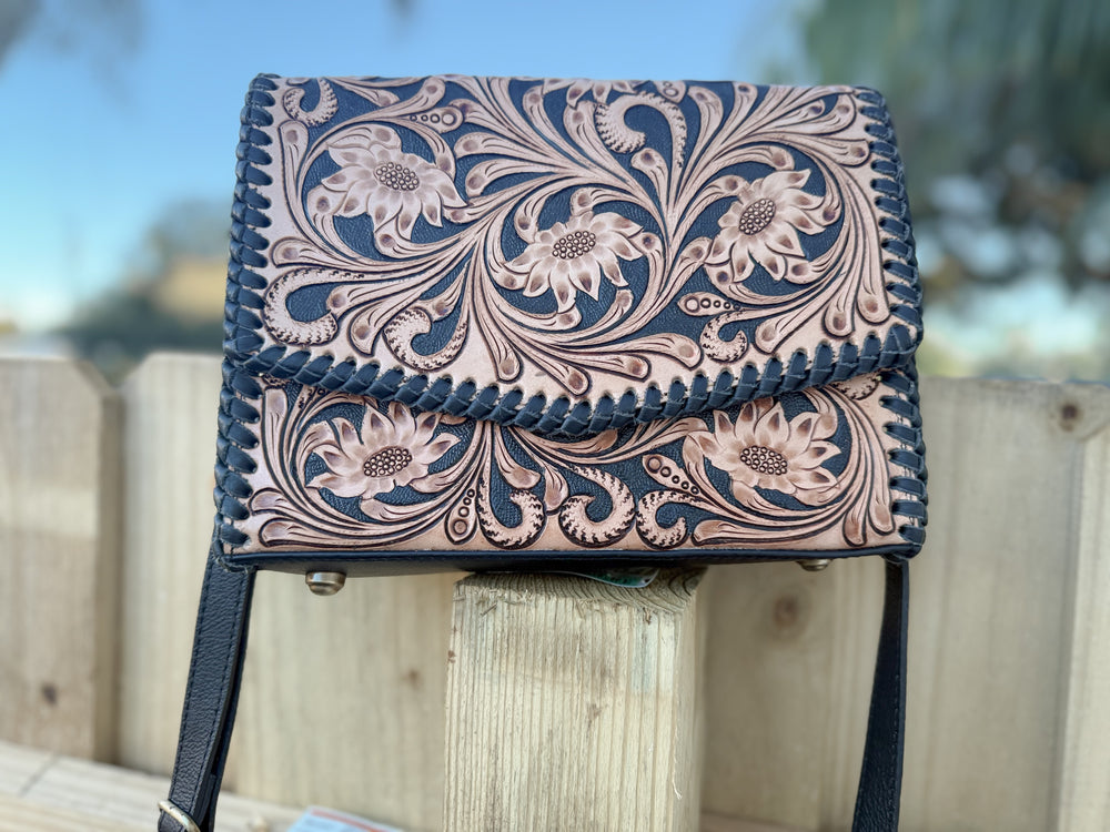 Tooled leather floral crossbody bag with black whipstitch edge and adjustable strap.