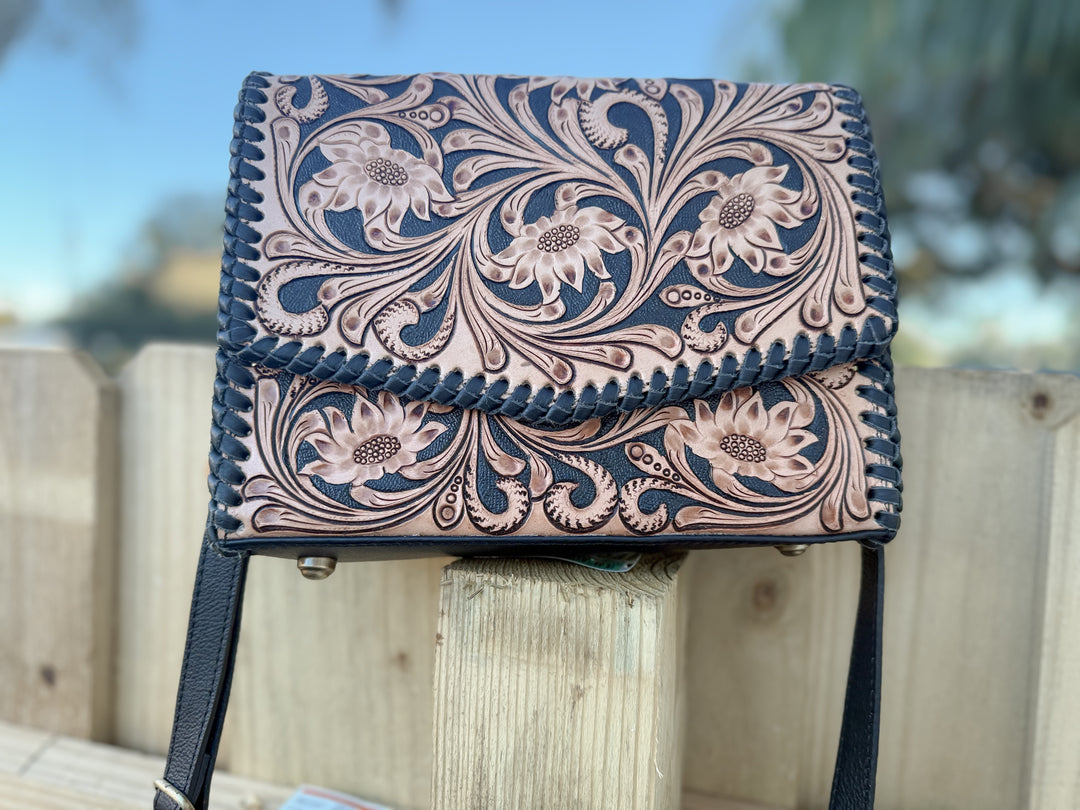 Tooled leather floral crossbody bag with black whipstitch edge and adjustable strap.