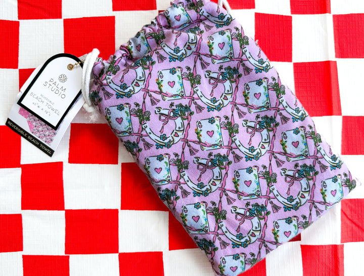 Pink reversible beach towel with western cowgirl print featuring playing cards, horseshoes, bows, and lucky icons on a red and white checkered background.