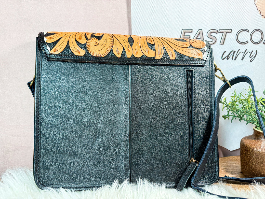 Black handbag with floral design on flap, showing exterior right zipper pocket for discreet carry placed on a white surface with a blurred background.