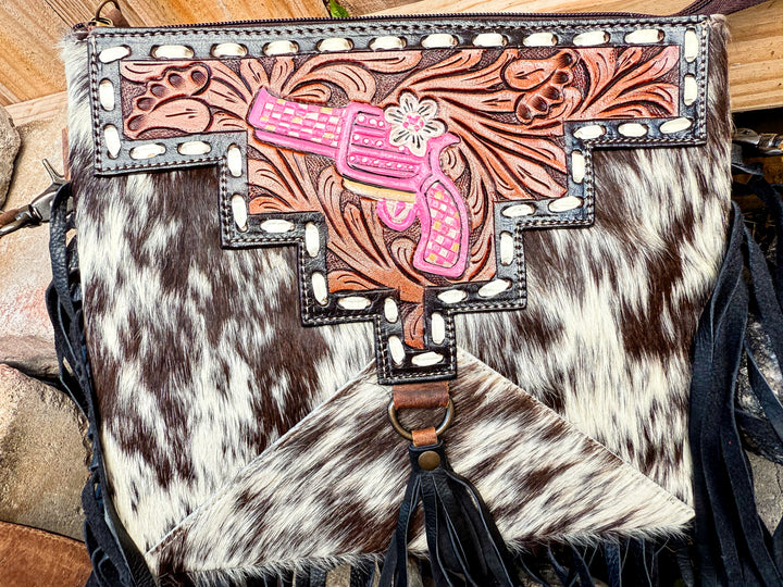 Cowhide bag with pink gun design and decorative elements on a wooden surface