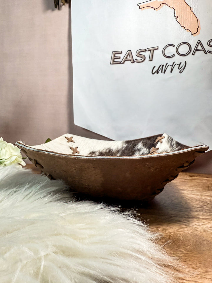 Decorative cowhide leather catch all bowl on a wooden surface, next to a white sign with 'East Coast Carry' text.