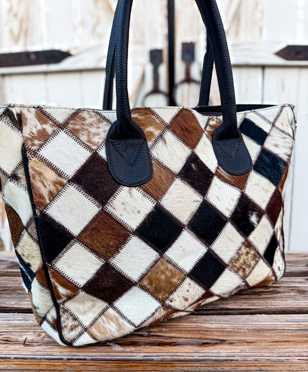 Checkered cowhide tote handbag with rich brown handles on a wooden surface