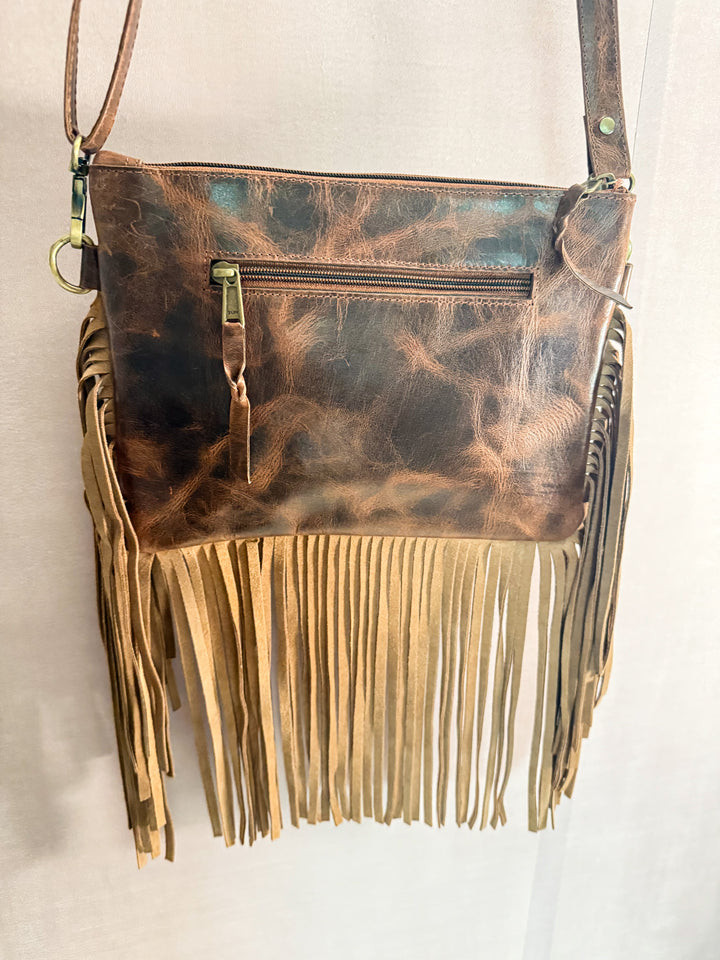 Backside of the Feral Grace Crossbody Brown full grain leather elegant western handbag with suede fringe details on a light background