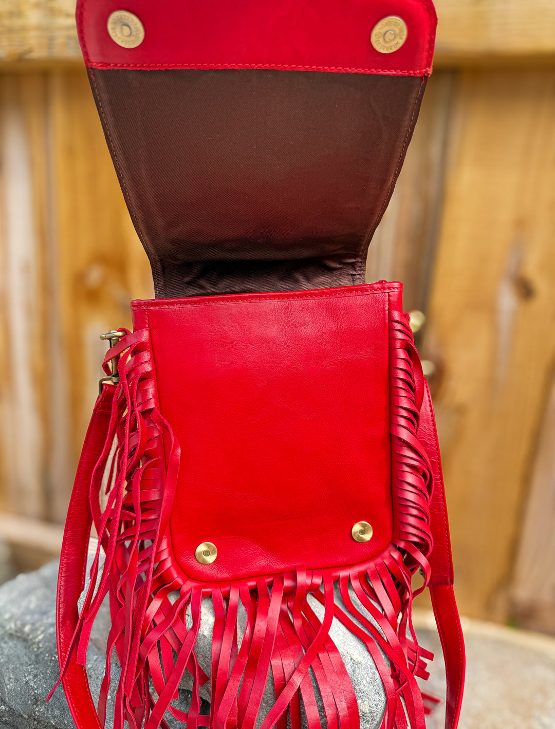 Inside view of red fringe crossbody bag with flap open showing snap button closure hardware and rich bright red leather 