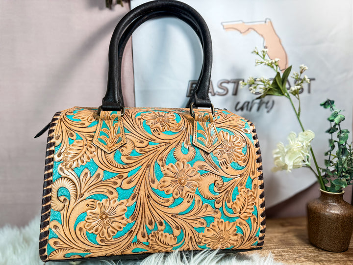 Back view of tooled leather western speedy satchel with smooth leather panel and black top handles