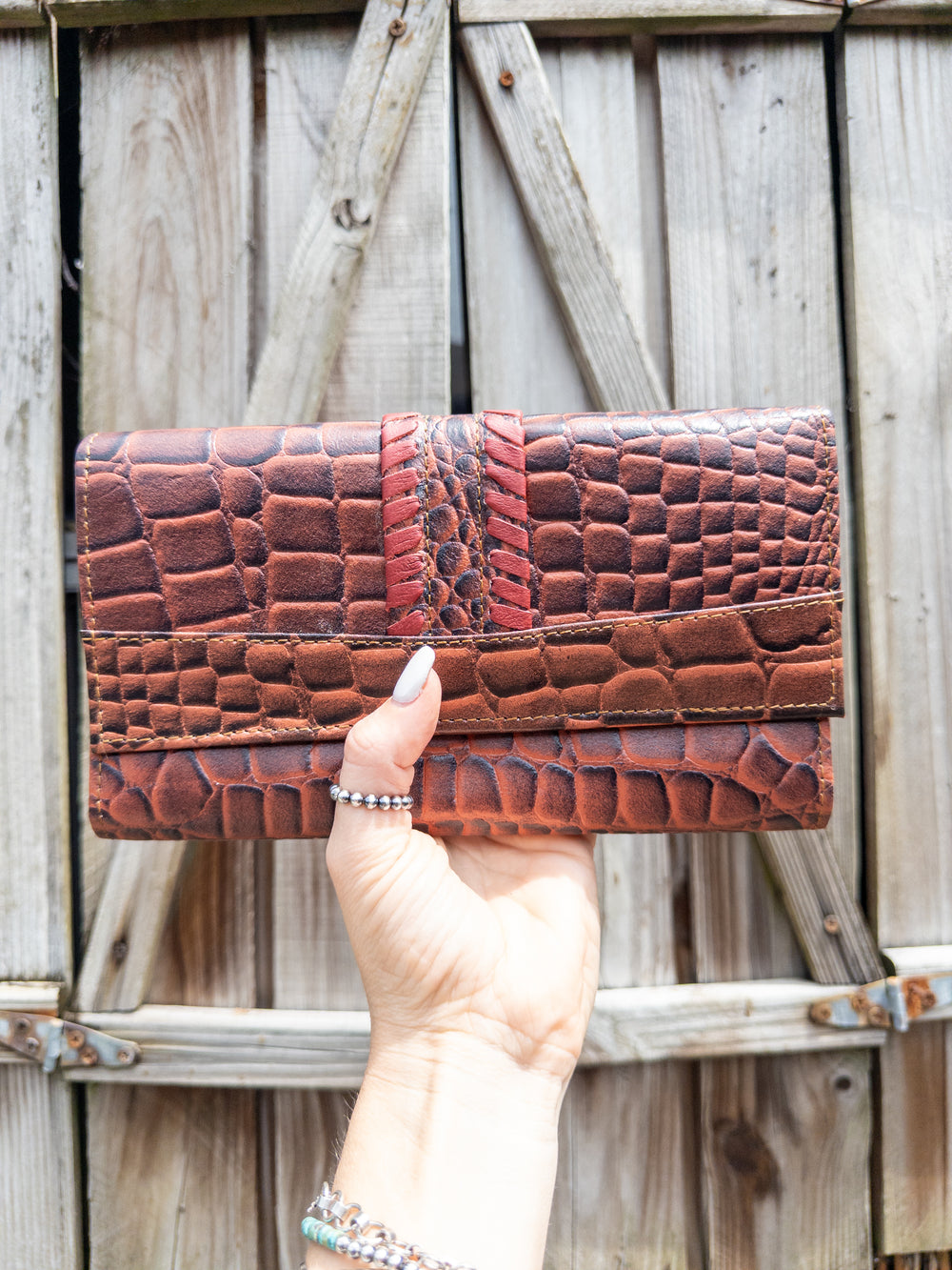 Embossed leather clutch wallet in croc-look pattern with bold red whipstitch detail, front view.