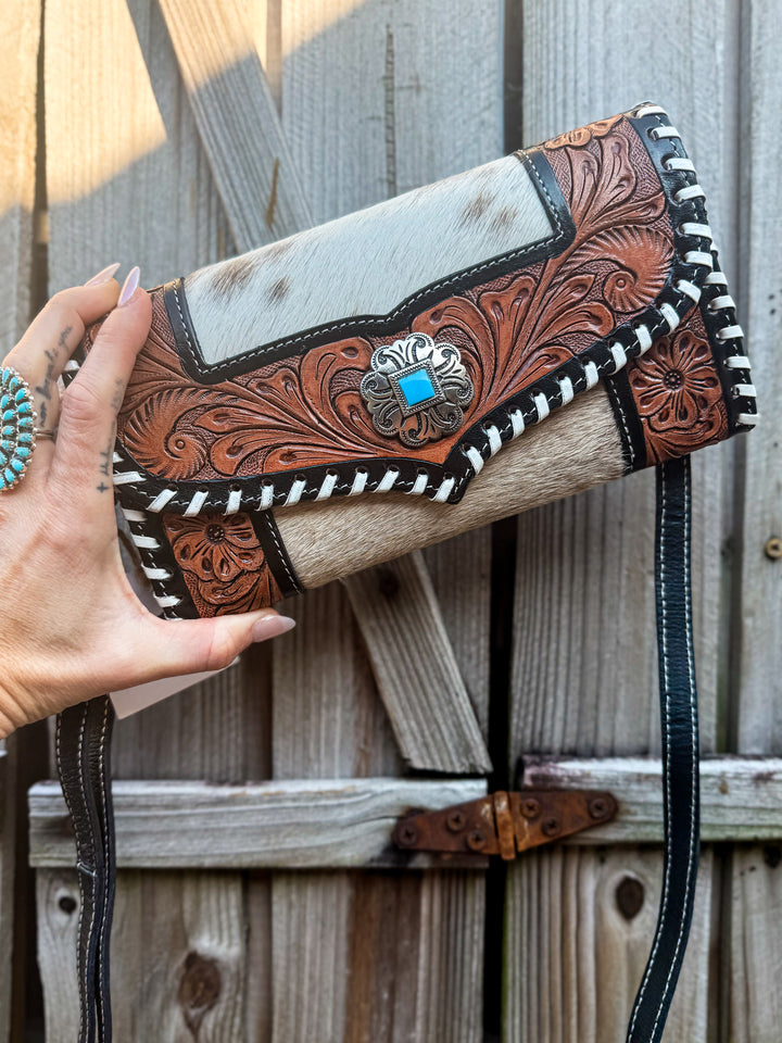 Handmade leather cowhide clutch with intricate leather designs held by a hand against a wooden background