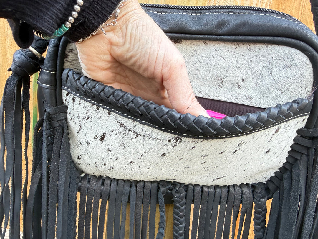 Hand showing front pocket view of Black cowhide fringe crossbody bag with braided leather strap