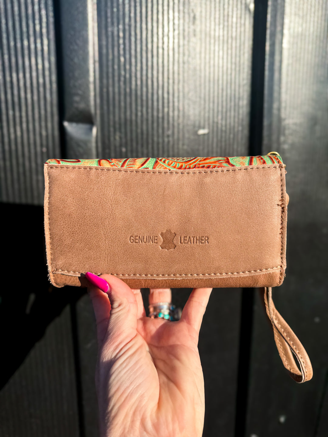 Brown leather wallet with 'Genuine Leather' label held by a hand against a dark background