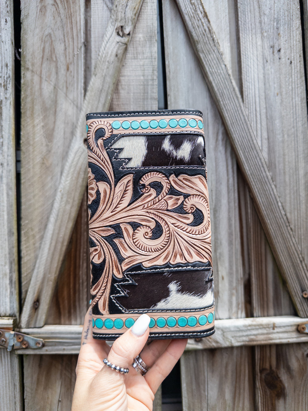Cowhide and tooled leather wallet with turquoise stud border, floral tooling, and natural hide pattern.