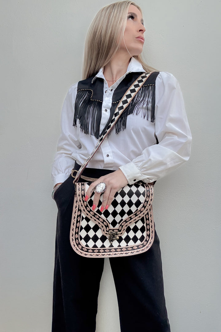 Woman holding a black and white checkered leather bag with tooling details against a plain background