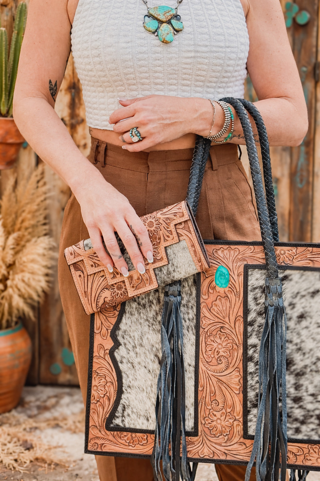 Woman holding a black and white speckled cowhide western concealed carry purse tote with black leather fringe and matching leather wallet 