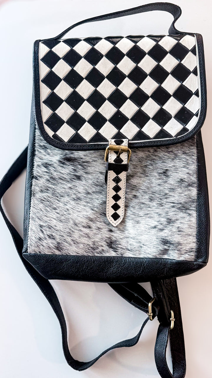 Speed Check black leather Western backpack with black and white diamond-patterned flap, salt-and-pepper cowhide front and buckle detail.