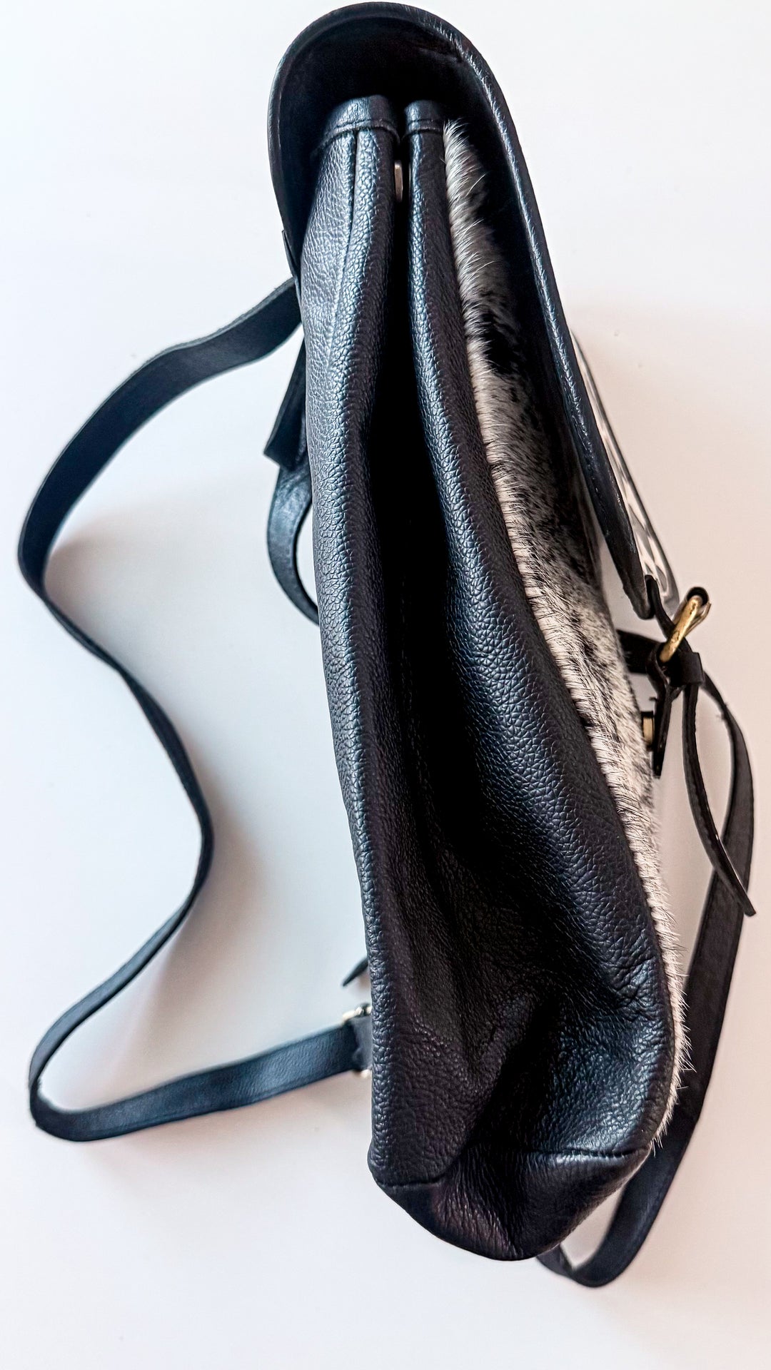 Side view of soft black leather cowhide backpack showing flexible construction, folded side panels and adjustable leather straps.