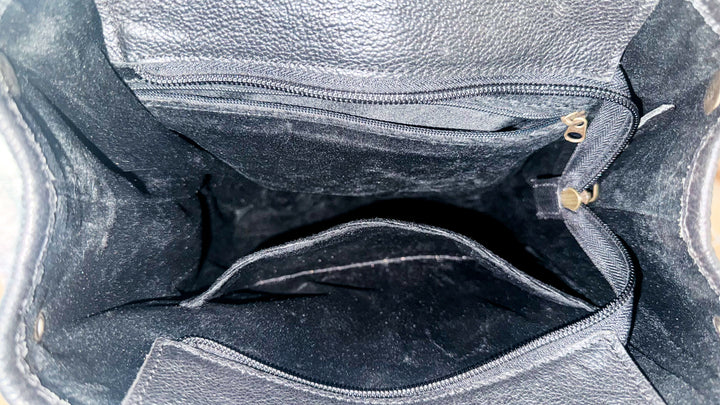 Interior of black leather cowhide backpack showing dark lining, zippered storage pocket, interior slip pocket and main compartment.