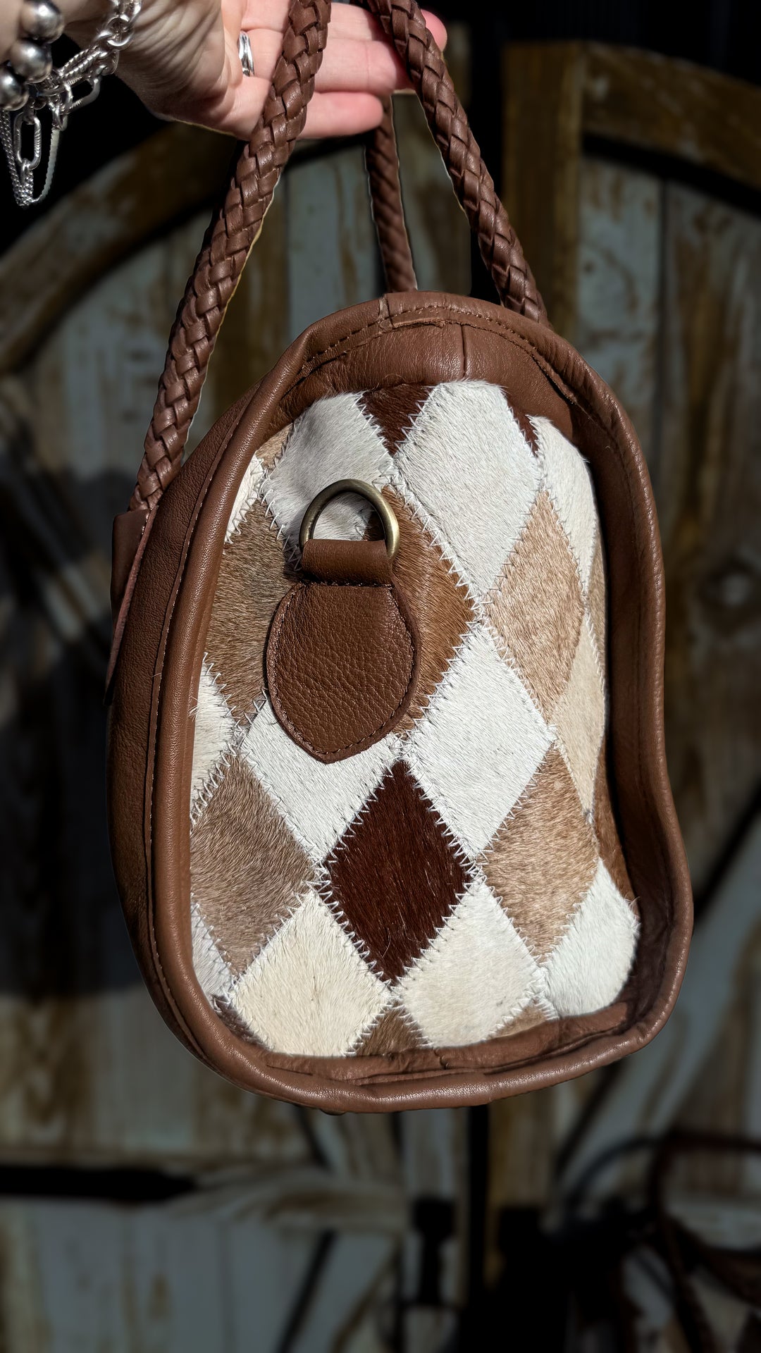 Side view of Soft & Strong cowhide satchel showing diamond patchwork hair-on hide, brown leather trim and metal strap attachment.